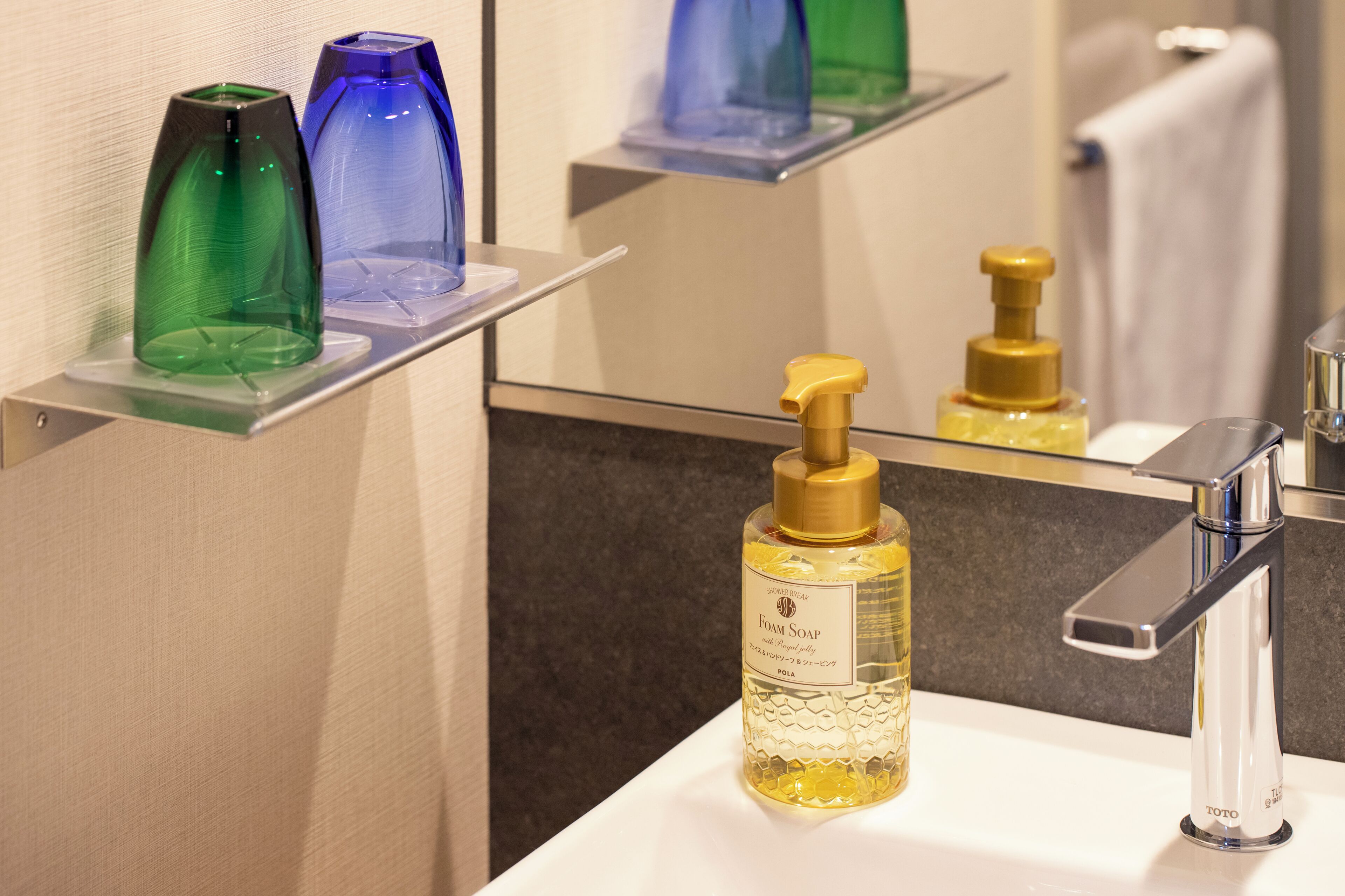 Une salle de bain avec un lavabo blanc, un miroir et une étagère sur laquelle sont posées trois bouteilles en verre.