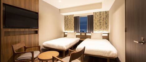 A hotel room with two single beds, a TV mounted on the wall, a wooden desk, and a chair.