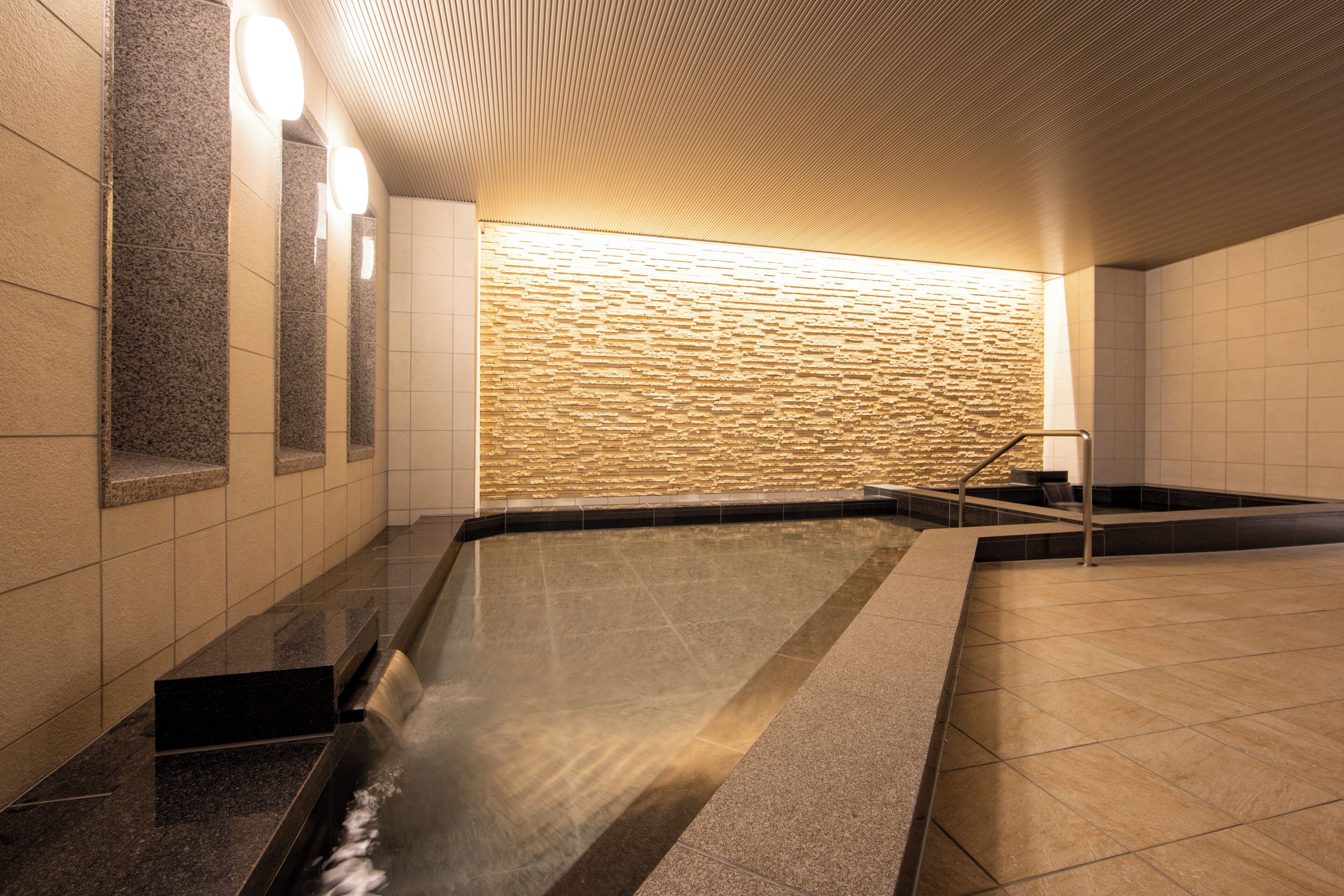 A modern indoor pool area with a stone wall and a clear water feature.