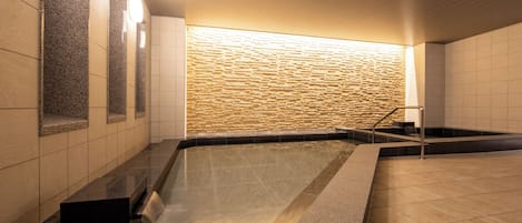 A modern indoor pool area with a stone wall and a clear water feature.