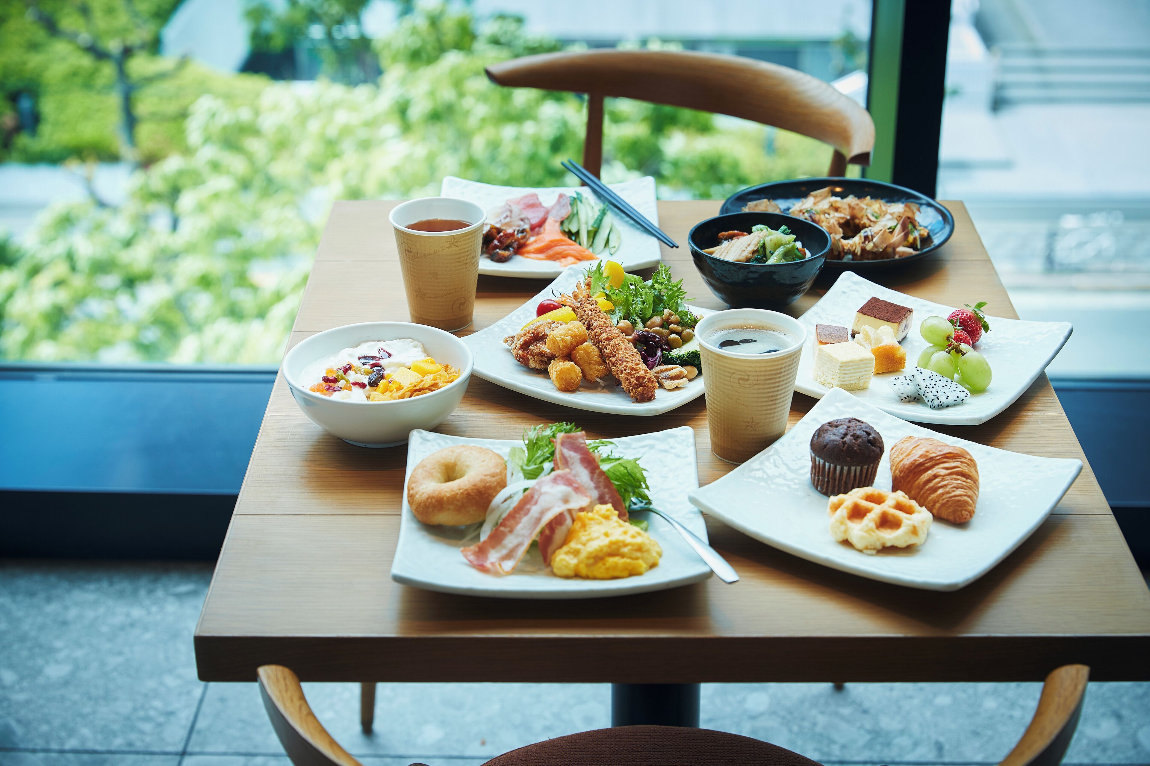 Una mesa de desayuno con diversos platos, como huevos, tocino, bollería y un bol de fruta.
