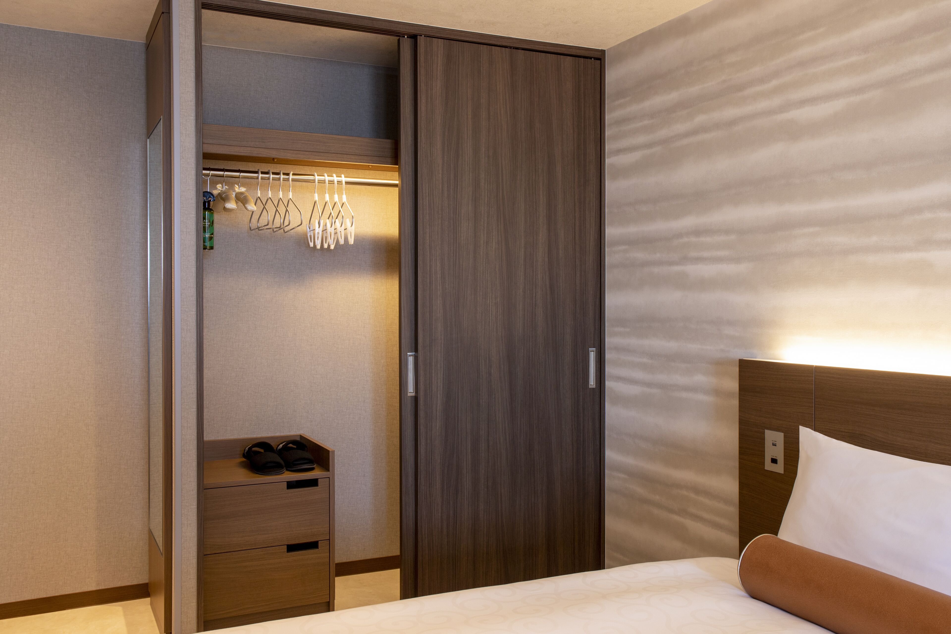 A hotel room with a bed, a wooden wardrobe, and a shoe rack.