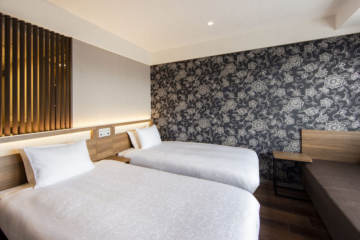 A hotel room with two beds, a wooden headboard, a patterned wallpaper, and a small wooden table.