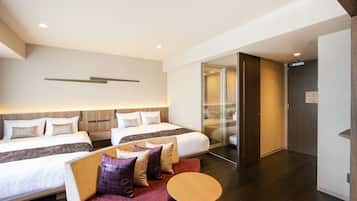 A hotel room with two beds, a sofa, a small table, and a glass door leading to a bathroom.