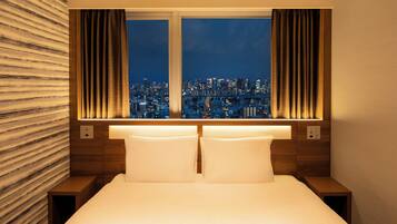 Habitación de hotel con cama, dos mesitas de noche, ventana con cortinas y vista a la ciudad.