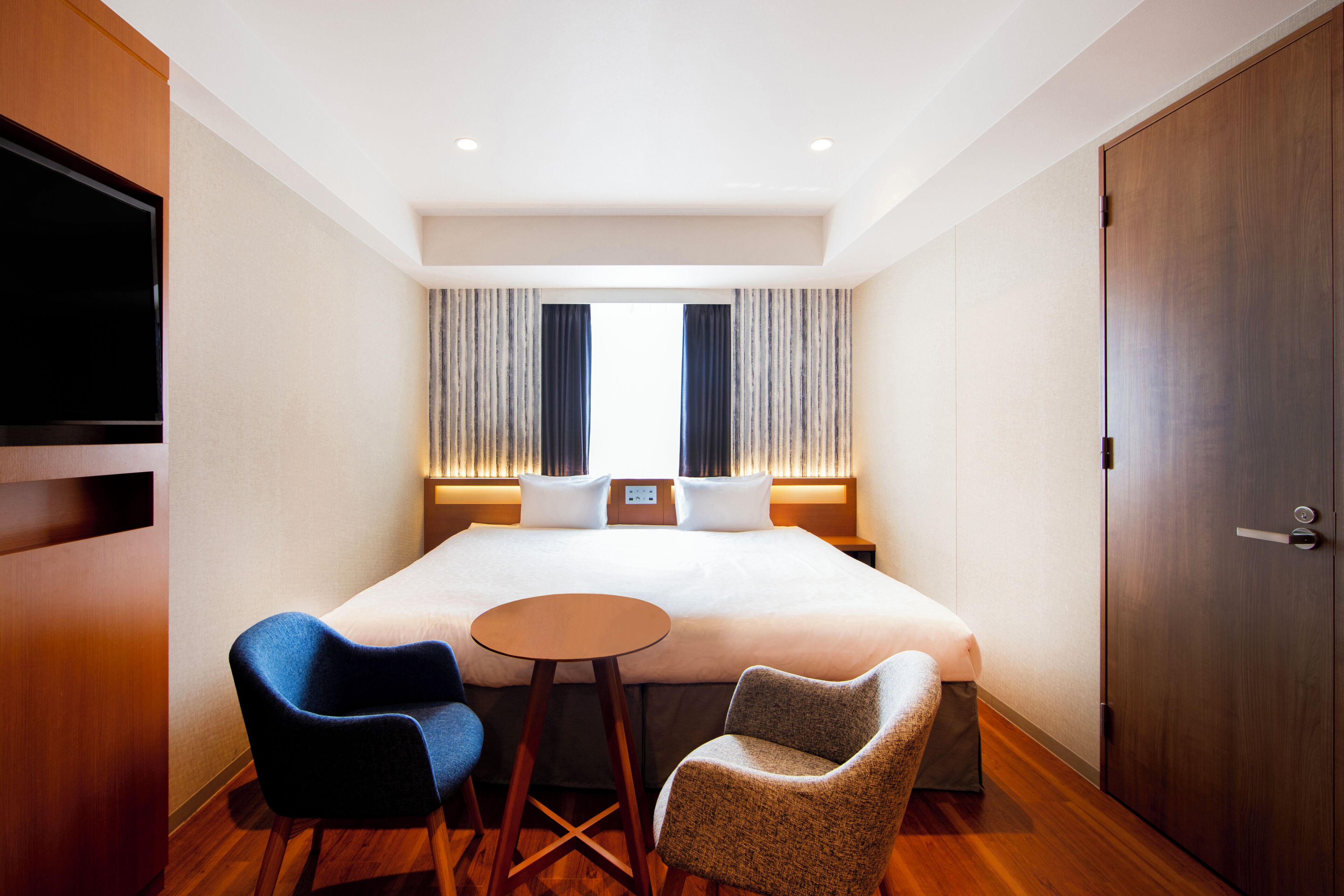 A hotel room with a large bed, two chairs, a small table, a TV, and a wardrobe.