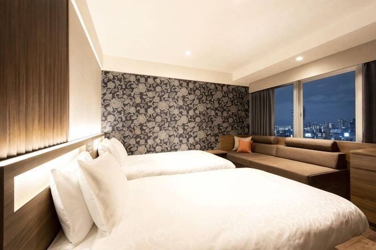 A hotel room with a large bed, a sofa, a city view, and a patterned wall.