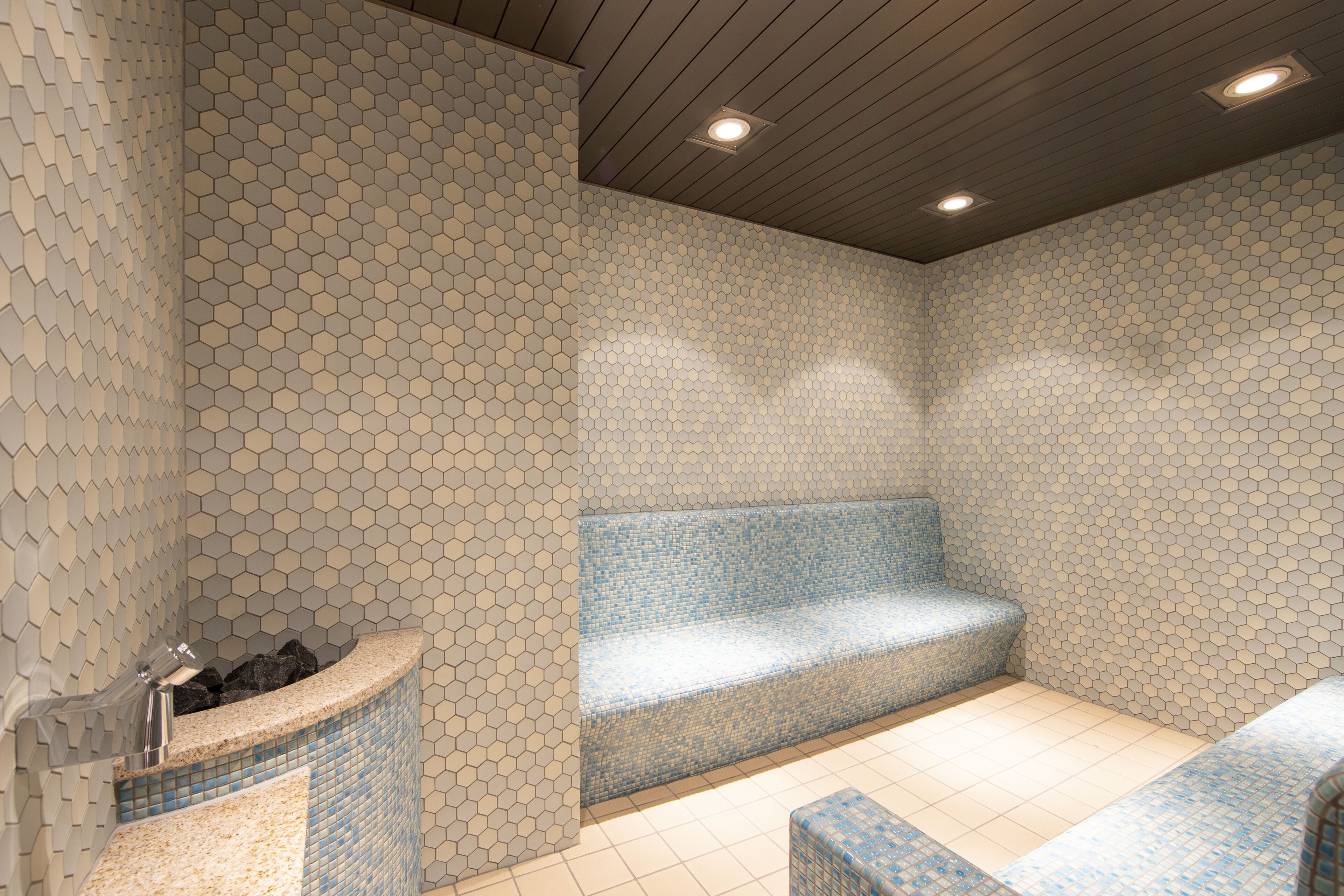 Une salle de bain moderne avec des murs recouverts de carreaux hexagonaux, un banc et un lavabo avec un robinet.