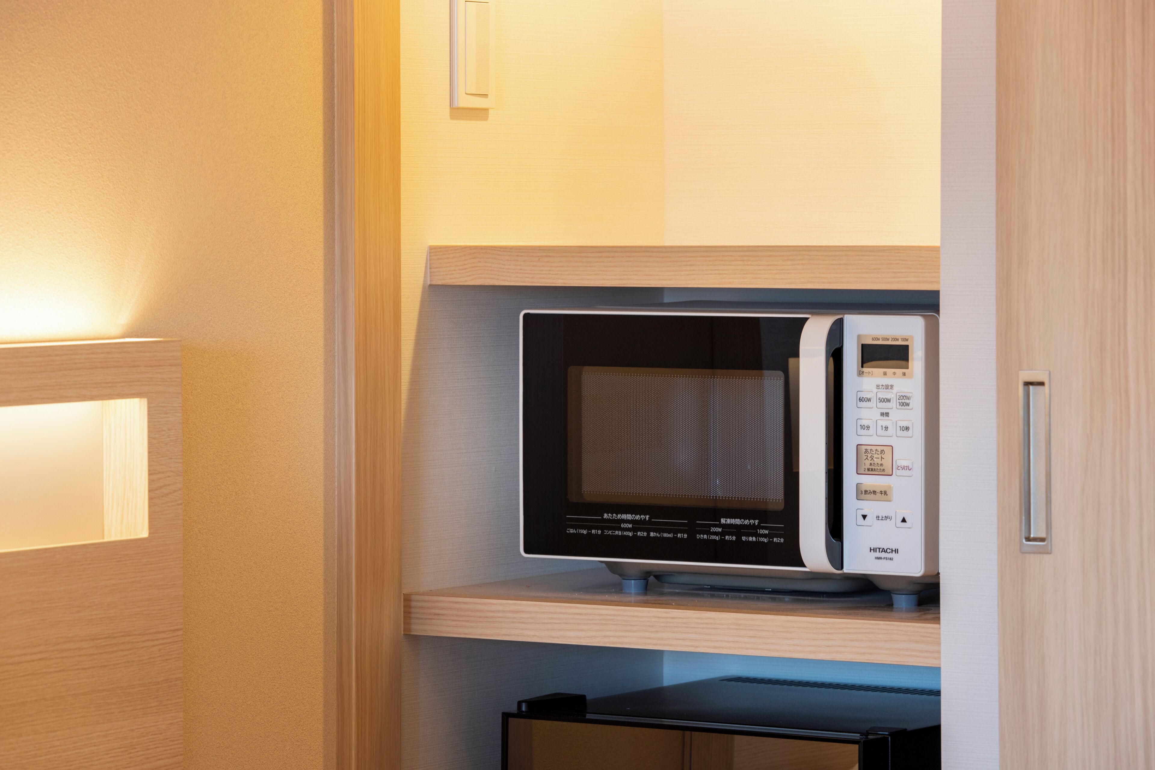 Un horno microondas con pantalla digital y panel de control, ubicado en un estante de madera dentro de un armario de cocina.