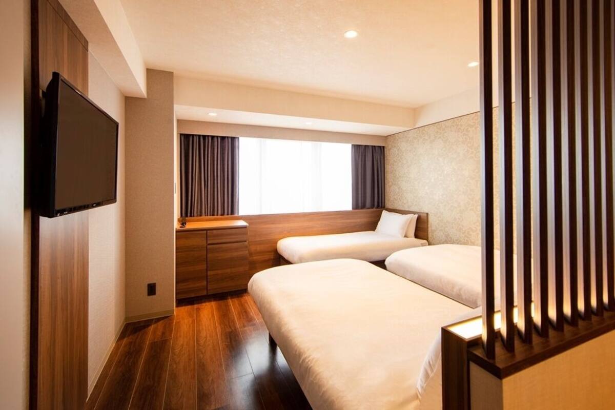 Habitación de hotel con dos camas, televisor, ventana con cortinas y suelo de madera.