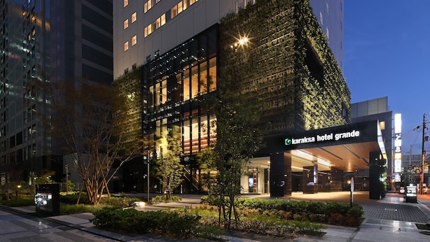 A modern hotel with a glass facade, a green vertical garden, and a well-lit entrance.