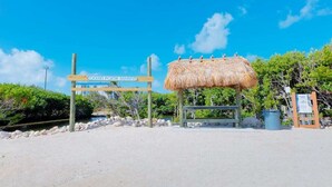 A beach entrance sign, a thatched hut, and a wooden bench. - Keys Waterfront Condo: Pool, Beach & Stunning Views! (Tavernier)