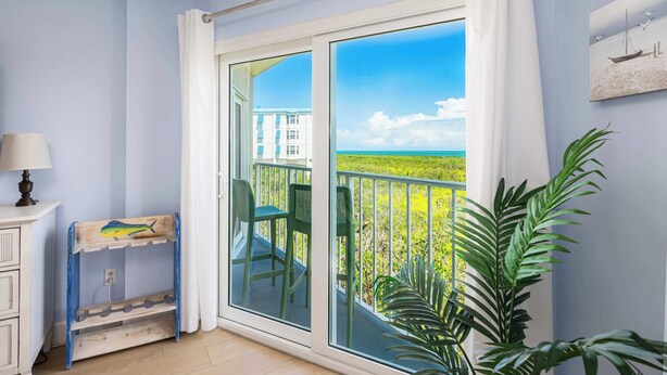 A room with a sliding glass door leading to a balcony with a view of a building and a green landscape. - Keys Waterfront Condo: Pool, Beach & Stunning Views! (Tavernier)