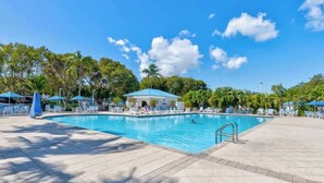 A swimming pool with lounge chairs and umbrellas, surrounded by palm trees and a pavilion. - Keys Waterfront Condo: Pool, Beach & Stunning Views! (Tavernier)