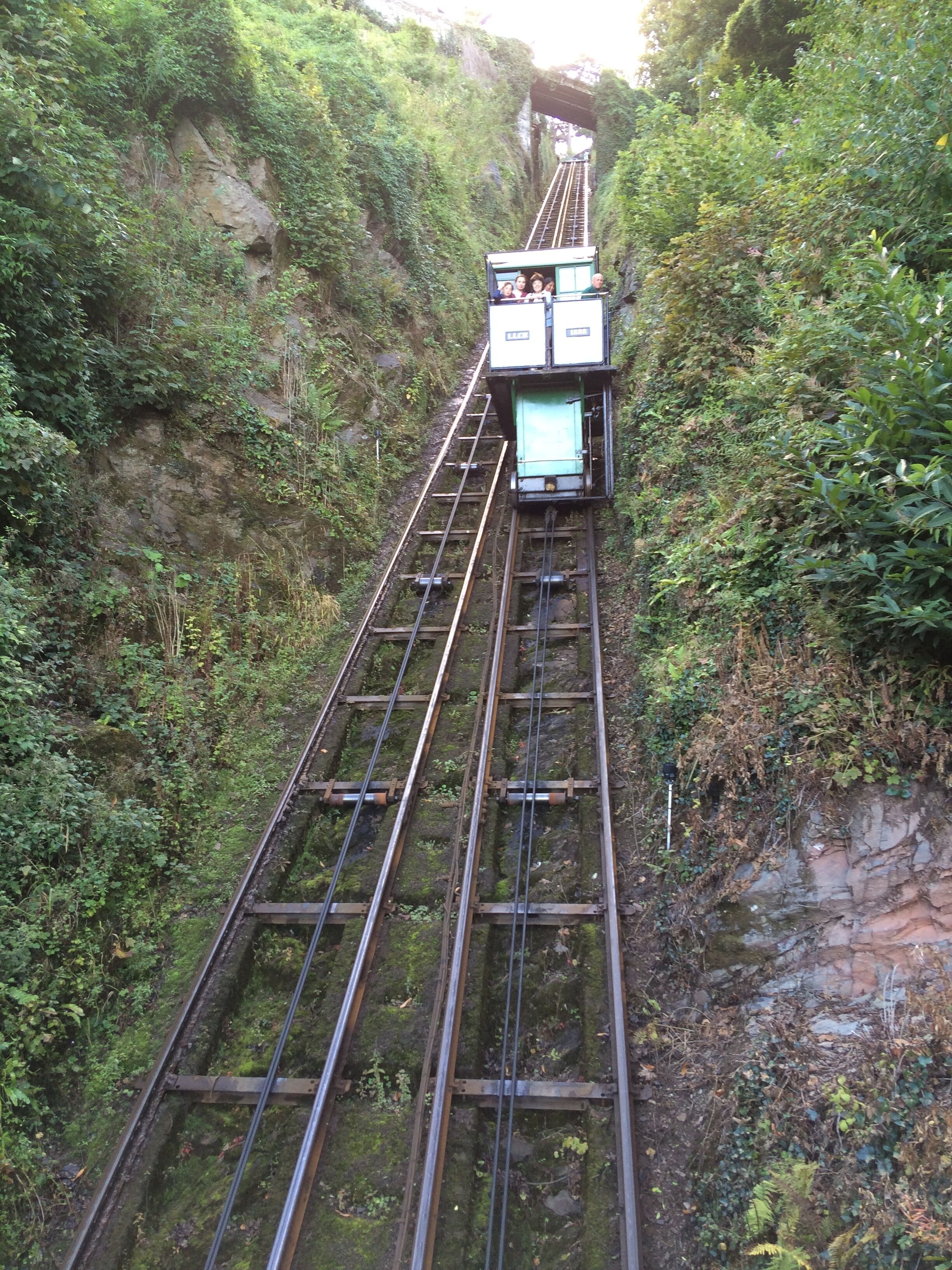 A cable car ascending a steep, rocky mountain path surrounded by dense greenery.