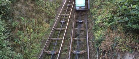 A cable car ascending a steep, rocky mountain path surrounded by dense greenery.