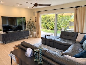 A modern living room with a large flat-screen TV, leather sofa, and a dining area with a table and chairs.