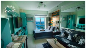 A compact living space with a bed, sofa, and kitchenette. A large window offers a city view. - Avida Towers Sucat (Parañaque)
