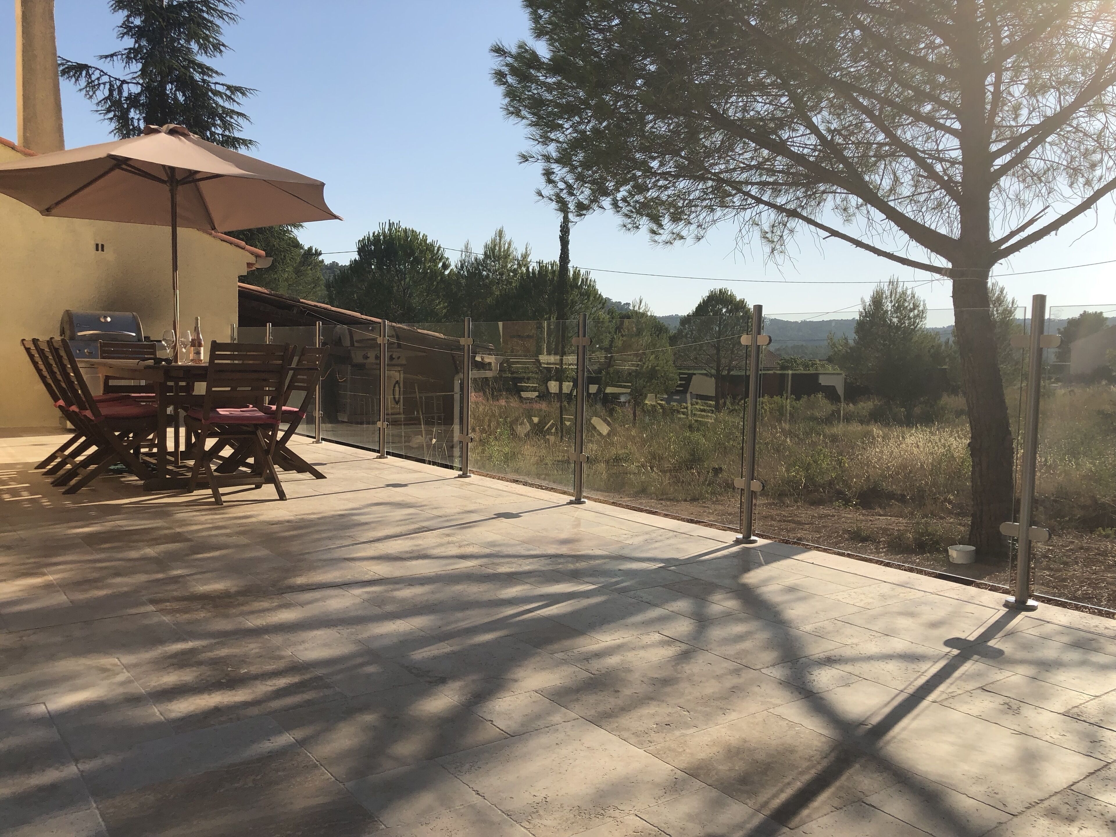 Eine Terrasse im Freien mit Tisch, Stühlen, einem Grill und Blick auf die umliegende Landschaft.