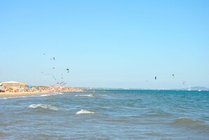Una playa con orilla arenosa, olas del océano y varios cometas volando en el cielo.