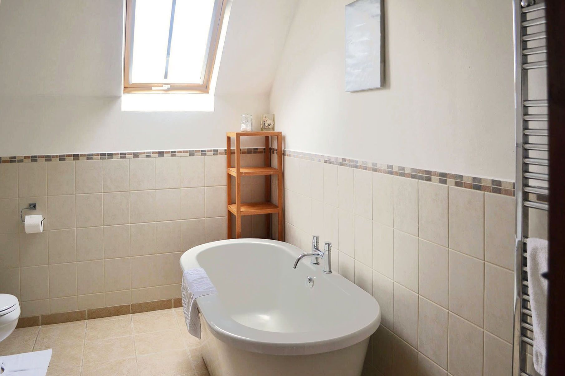 Une salle de bain avec une baignoire sur pieds, une étagère en bois et une fenêtre laissant entrer la lumière naturelle.