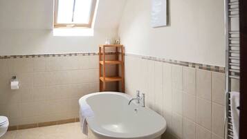 Une salle de bain avec une baignoire sur pieds, une étagère en bois et une fenêtre laissant entrer la lumière naturelle.