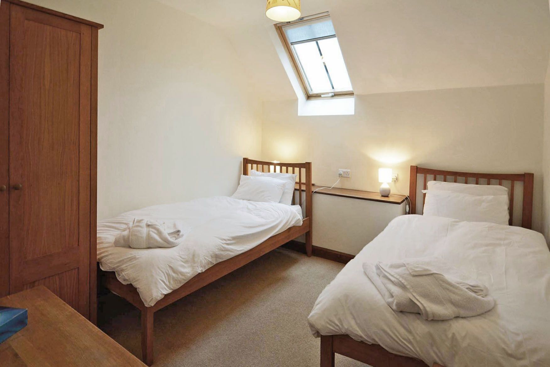 A bedroom with two single beds, a wooden wardrobe, a desk, and a skylight.