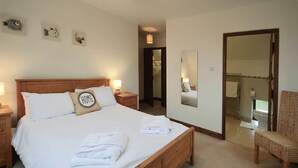A bedroom with a wooden bed, white bedding, a "HOME" pillow, bedside lamps, a chair, a mirror, and a bathroom visible through an open door.