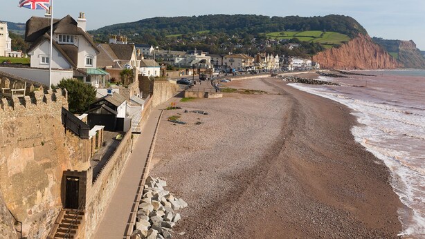 A coastal town with a pebbly beach, stone walls, and houses along the shore.