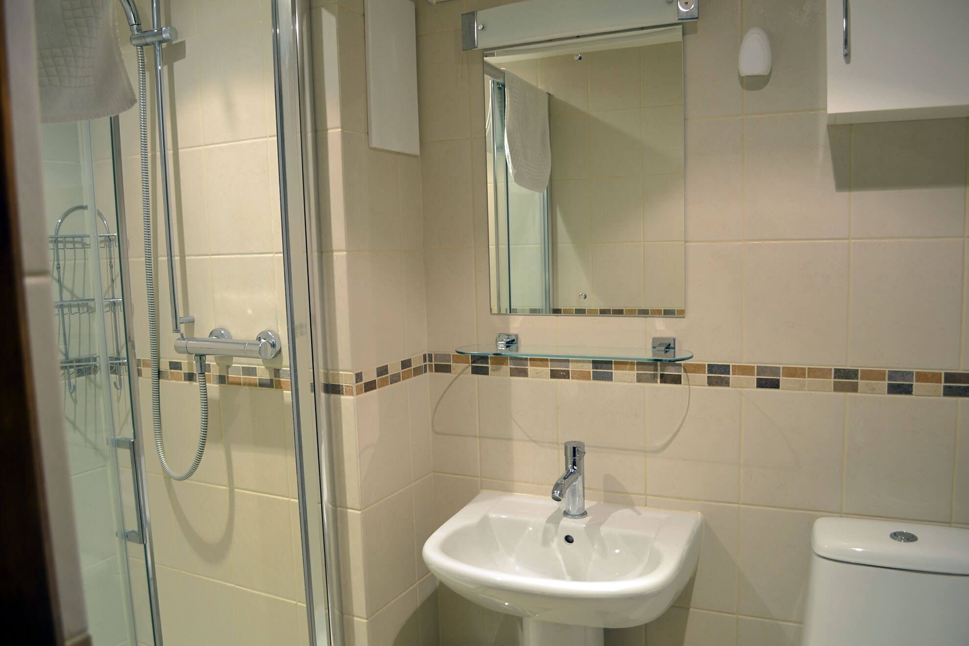 Een badkamer met een douchecabine van glas, een wit wastafelmeubel en een toilet.