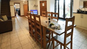 A spacious dining area with a wooden table and chairs, a television in the background, and a kitchen area with cabinets and a sink.