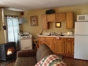 Cozy living room with a fireplace, sofa, and TV. Features a kitchen area with a stove, sink, and refrigerator.