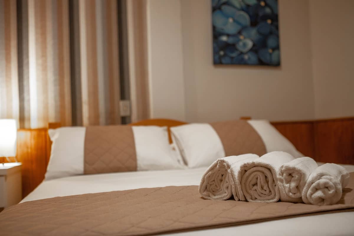 A neatly made bed with rolled towels, a wooden headboard, and a painting on the wall.