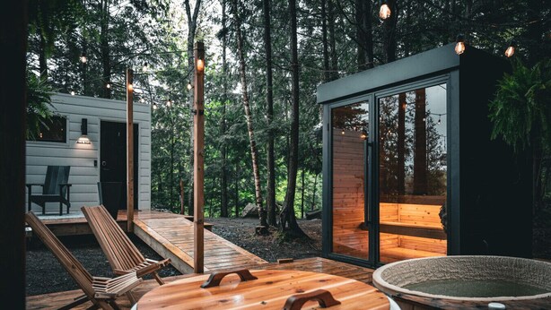 A modern cabin with a wooden deck, a hot tub, and a sauna.