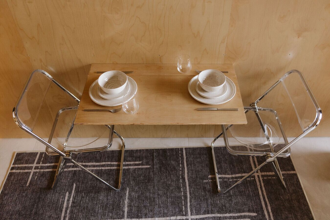 Una mesa de madera con dos platos blancos y un vaso, flanqueada por dos sillas de cromo.