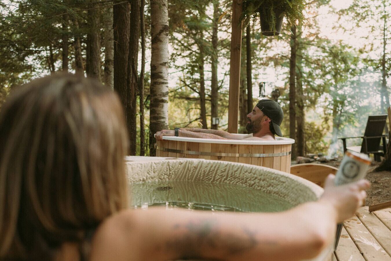 En person holder en drink i nærheden af en jacuzzi i et skovområde.