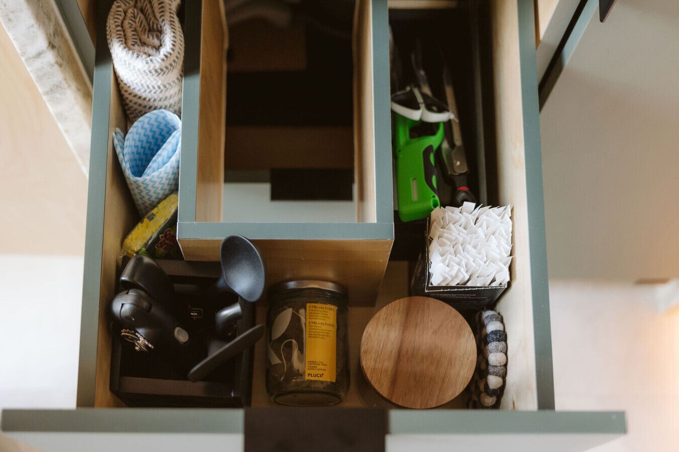 A drawer with various items including a jar labeled 'PLUCK', a wooden bowl, a black object, a green tool, and a blue and white patterned item.