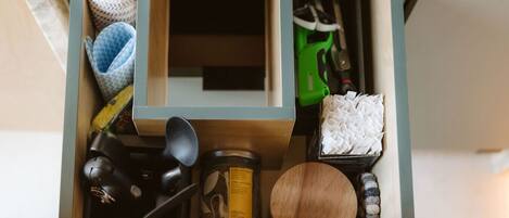 A drawer with various items including a jar labeled 'PLUCK', a wooden bowl, a black object, a green tool, and a blue and white patterned item.