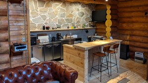 A cozy log cabin interior with a stone wall, wooden furniture, a bar area, and a leather couch. - Log cabin rental & Finland Sauna Step House (Yamanakako)