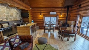 A log cabin interior with a stone wall, wooden furniture, a kitchen area, and a dining table. - Log cabin rental & Finland Sauna Step House (Yamanakako)