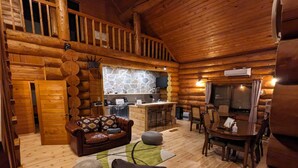 A log cabin interior with a cozy living area, a stone fireplace, a kitchen, and a dining table. - Log cabin rental & Finland Sauna Step House (Yamanakako)