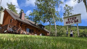 A rustic log cabin with a 'Step House' sign, surrounded by lush greenery and trees. - Log cabin rental & Finland Sauna Step House (Yamanakako)