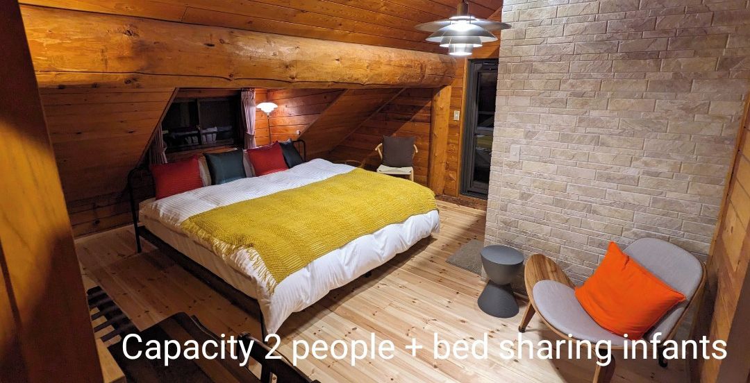 Una habitación acogedora con una cama, una silla y una mesita pequeña. Las paredes son de madera y el techo es inclinado.