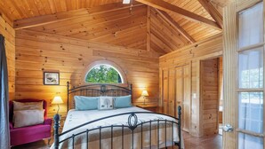 A wooden cabin bedroom with a bed, a window, a door, and a chair.