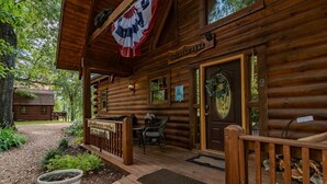 A wooden cabin with a porch, a dining area, and a door with a bear emblem.