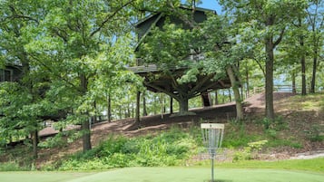 A treehouse structure built into a large tree, surrounded by lush greenery and a golf course.