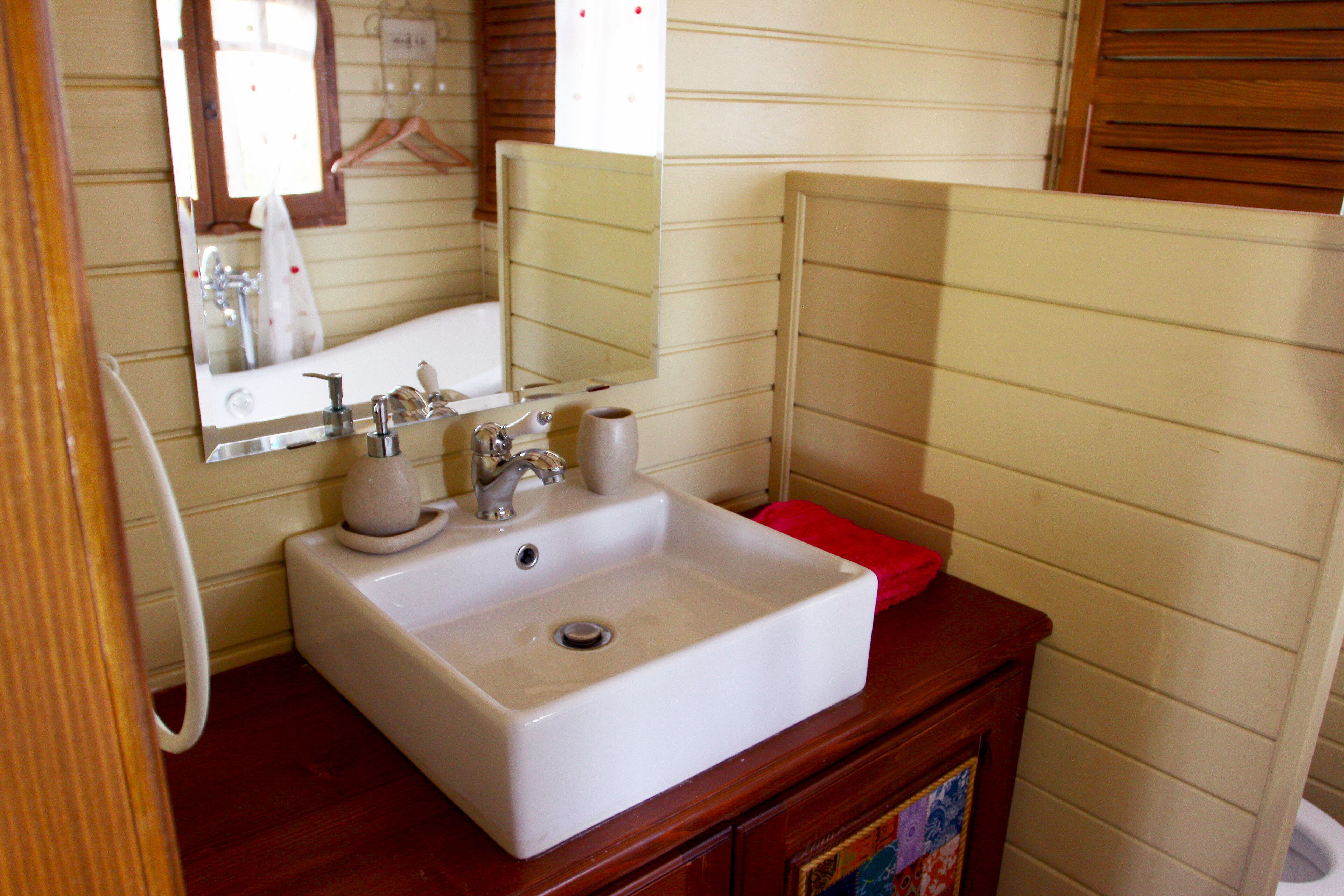 Un baño con lavamanos blanco, espejo y tocador de madera.