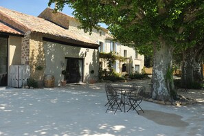 A courtyard with a stone building, a table with chairs, and a large tree providing shade. - CHARMING GUEST HOUSES IN PROVENCE IN THE HEART OF THE VINES (Sarrians)