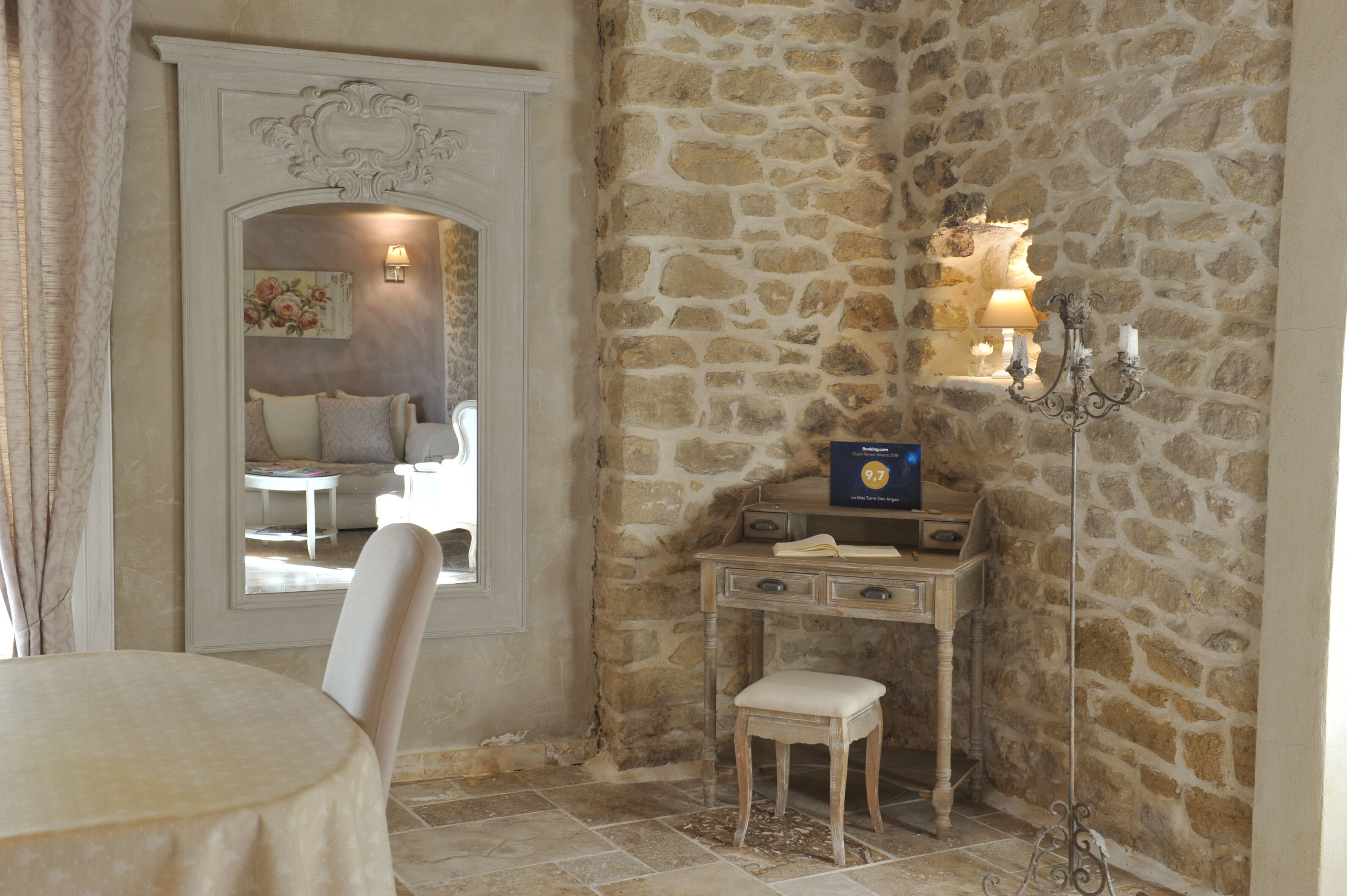 Une pièce avec un mur en pierre, un bureau en bois doté de tiroirs, un petit tabouret et une table avec une chaise.