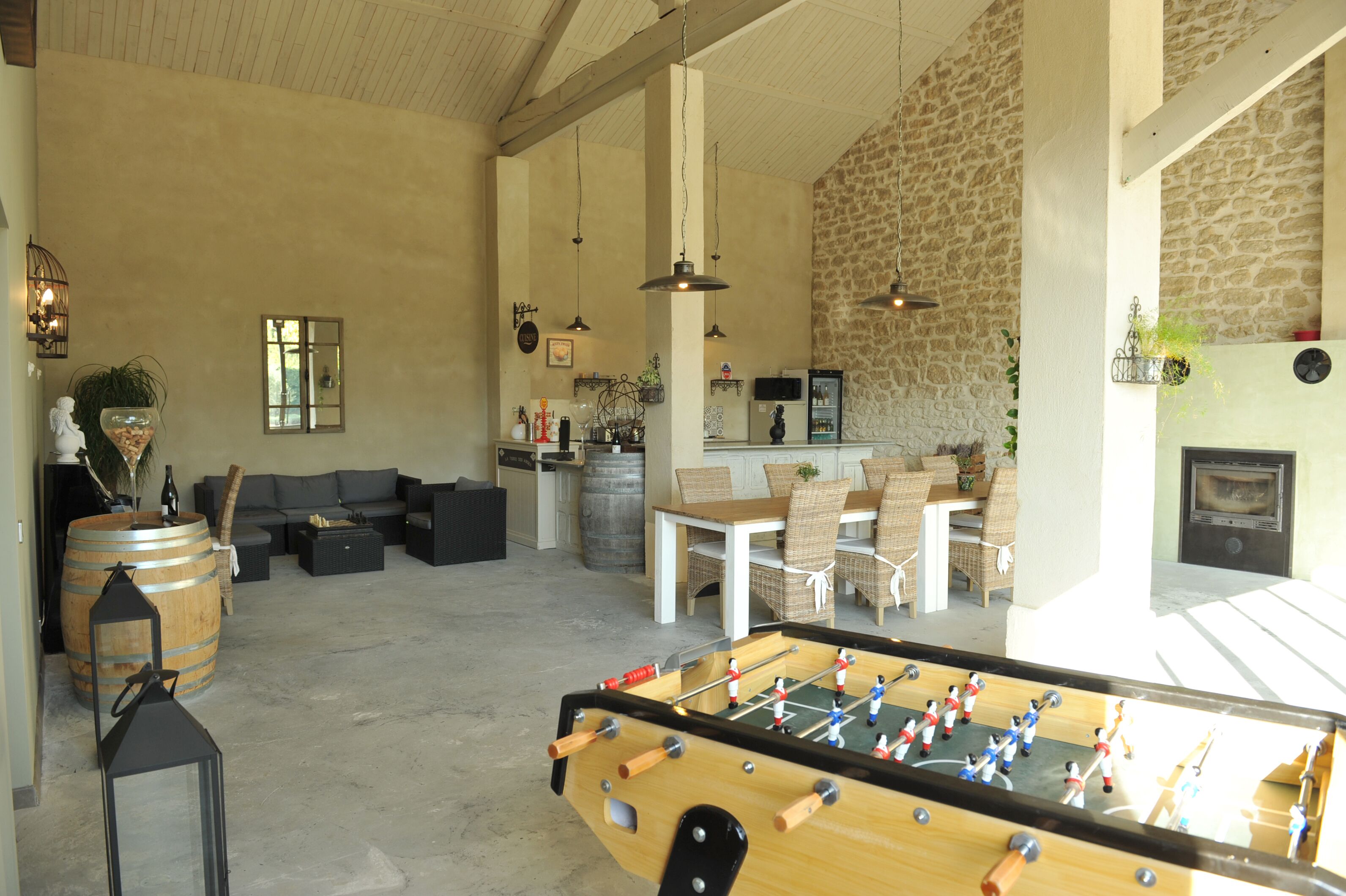 A spacious living area with a foosball table, comfortable seating, a kitchen area, and a stone wall.